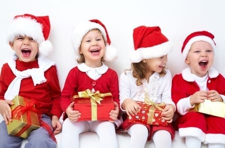 cute kids sitting with presents dressed up in santa clause outfits